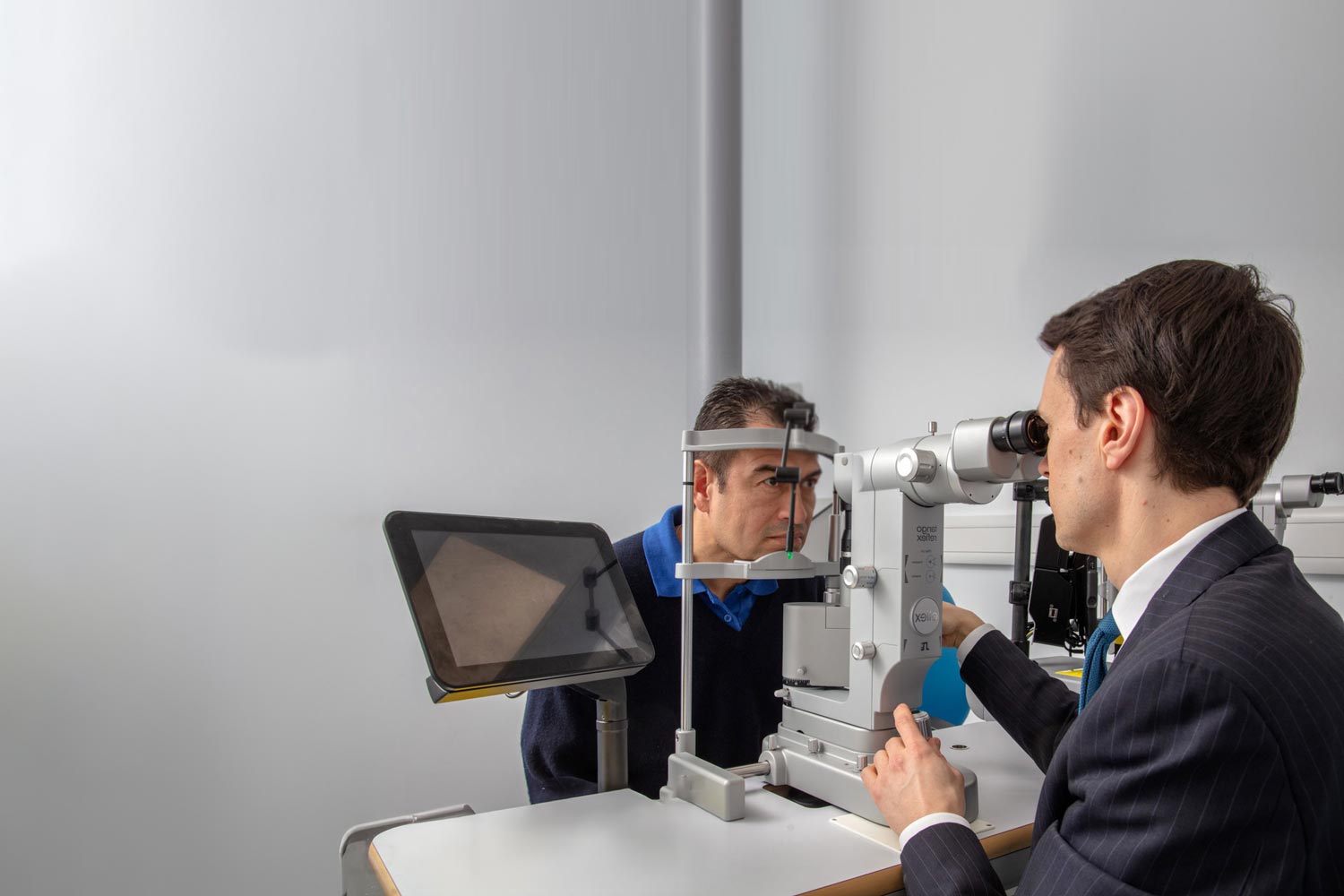 Mr James E. Neffendorf conducting an eye examination on a male patient using a specialised slit lamp in a medical office.